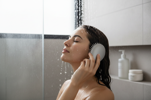 Persona usando cepillo de masaje en la cabeza bajo la ducha